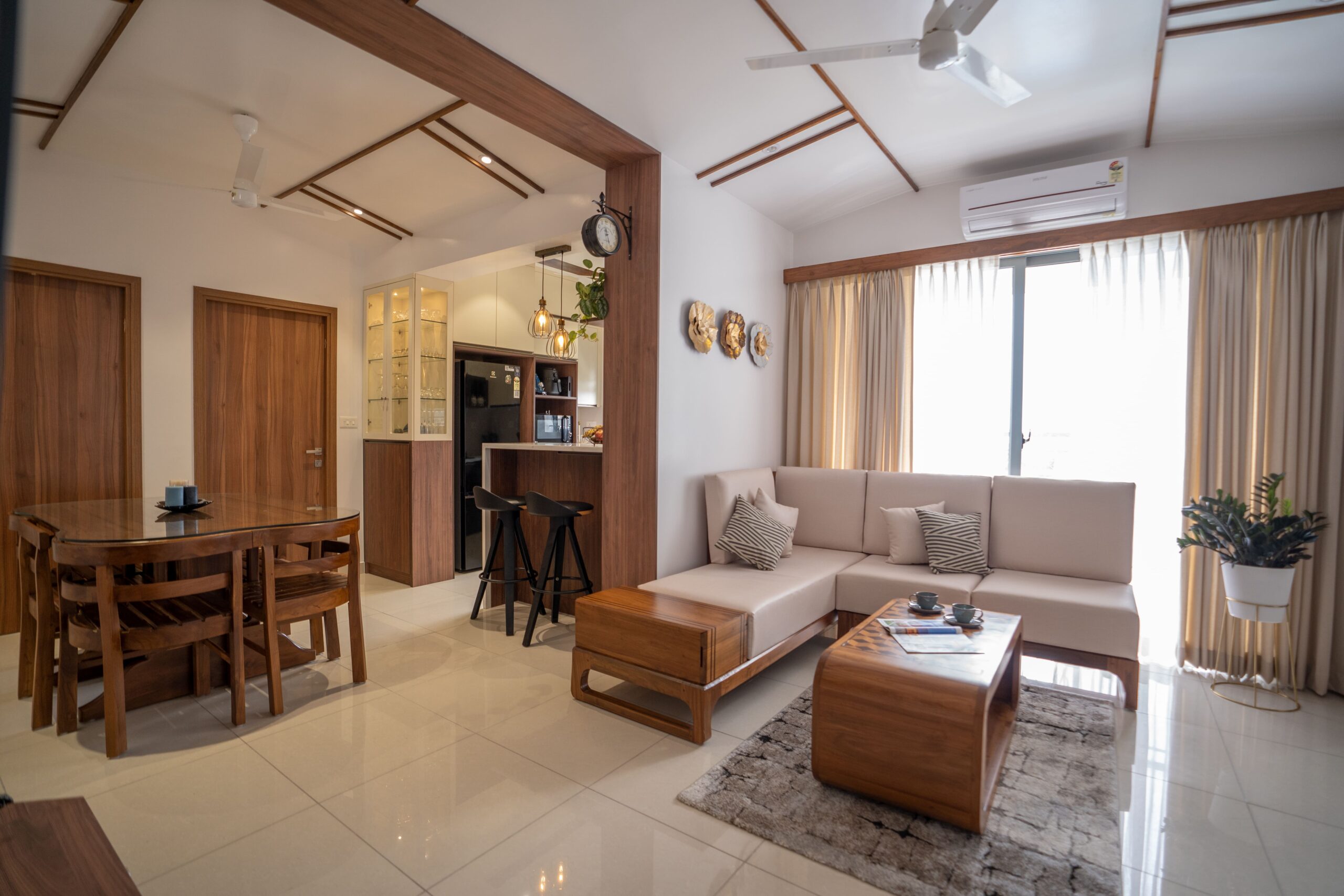 Modern residential interior design by Lykke Architecture Studio featuring a warm wood-toned living and dining area, an L-shaped sofa, and a minimalist breakfast bar with industrial pendant lighting.